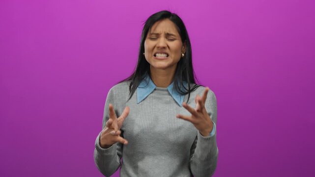 Woman expressing frustration with eyes closed on pink background wearing gray sweater.