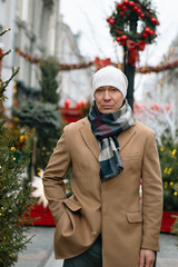 Winter portrait of adult caucasian man wearing beige coat at Christmas festive decorated modern city. Cold winter weather.