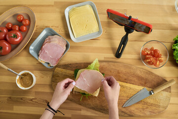 Young girl preparing sandwich with ham, cheese, lettuce and peanut butter while recording video on...