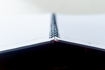 A close-up angled shot of an open spiral-bound notebook. The clean, white, lined pages are empty. Perfect background for study or notes.
