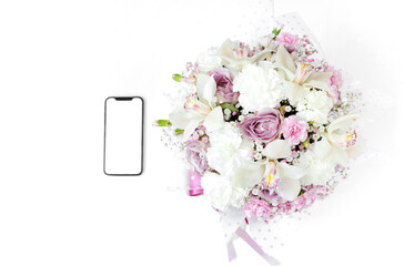 A phone with a white screen lies near the flowers isolated on a white background. The concept of online shopping. A gift for beloved woman. International Women's Day. Concept of love