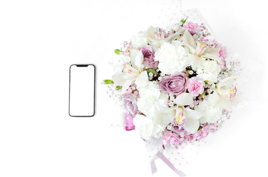 A phone with a white screen lies near the flowers isolated on a white background. The concept of online shopping. A gift for beloved woman. International Women's Day. Concept of love