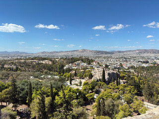 Panoramic view of Athens framed by lush cypress trees and mountains beneath clear blue skies.
