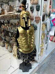 Golden Roman centurion armor and helmet with plume displayed in a Greek souvenir shop — historical costume texture.