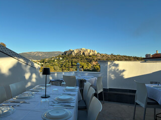 View of the Acropolis and Parthenon from a bright restaurant terrace on a sunny day in Athens.