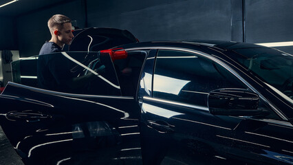 Worker drying car interior door frame with red air blower during detailing. Concept of precision, care, and workflow control in professional vehicle maintenance.