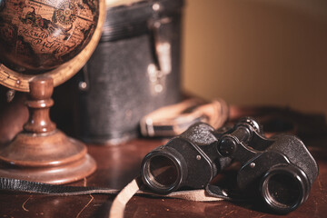 Binoculars on a table, with a leather case and a wooden globe 
