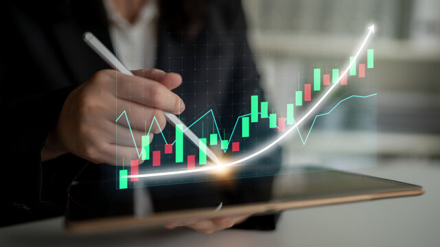 A professional individual analyzes a stock market graph on a digital tablet, showcasing business indicators and data visualizations in a modern office setting. Impute - Powered by Adobe