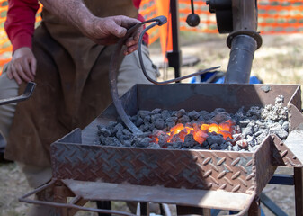 Blacksmith working with glowing coals and metal tools at outdoor forge