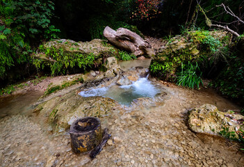 Wide angle view of a serene natural pool with crystal clear turquoise water formed by travertine rocks in a hidden forest canyon surrounded by lush vegetation