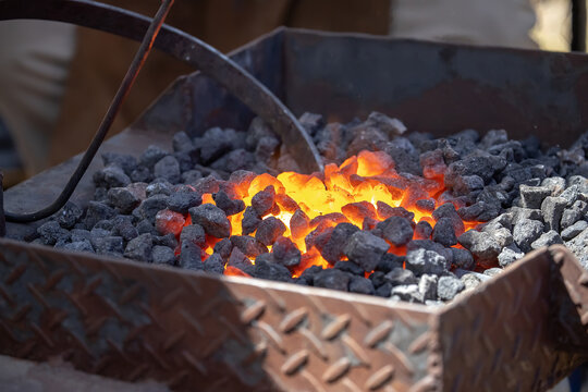 Blacksmith working with glowing coals and metal tools at outdoor forge