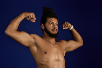 Sportive man flexing muscles during workout against a vibrant blue background