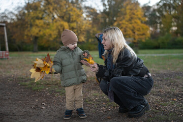 A Child Holding Bright Autumn Leaves While Interacting with a Caregiver in a Serene Outdoor Setting Surrounded by Golden Trees