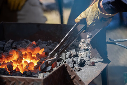 Blacksmith working with glowing coals and metal tools at outdoor forge