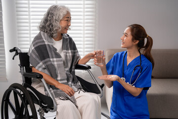 Asian nurse caregiver provides medication water older patient wheelchair home care medical assistance
