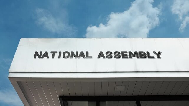 A National Assembly word sign displayed on a large, formal government building under a clear blue sky, symbolizing national legislature, governance, and democratic policy