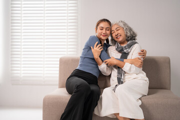 Asian young adult daughter older mother happy embrace together sofa home setting showing love support care intergenerational bond family wellbeing retirement comfort peaceful moments