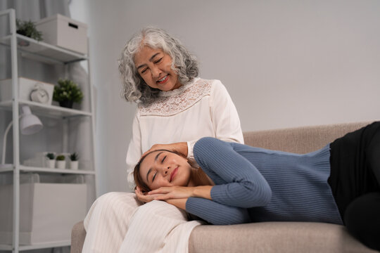 Asian older and young adult women share tender moment comfort support living room home gentle touch head on lap peaceful relaxation