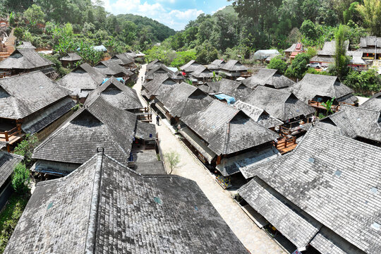 Aerial view of the village with dark, thatched roofs create a textured tapestry against the verdant green hills, Nuogang Village, Yunnan, China.