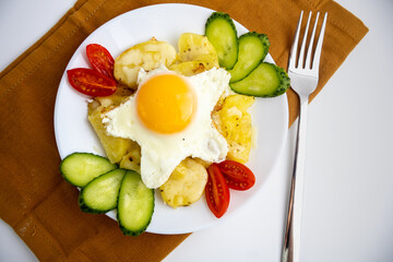 Fried potatoes with vegetables and an egg on a plate on a brown towel and a white background