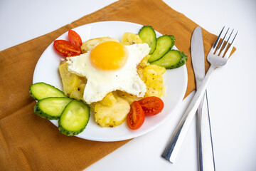 Fried potatoes with vegetables and an egg on a plate on a brown towel and a white background