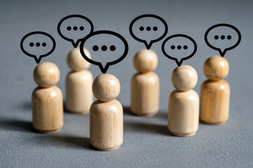 A Close-Up Photograph of Several Small Wooden Peg People Figures with Speech Bubble Icons Above Their Heads