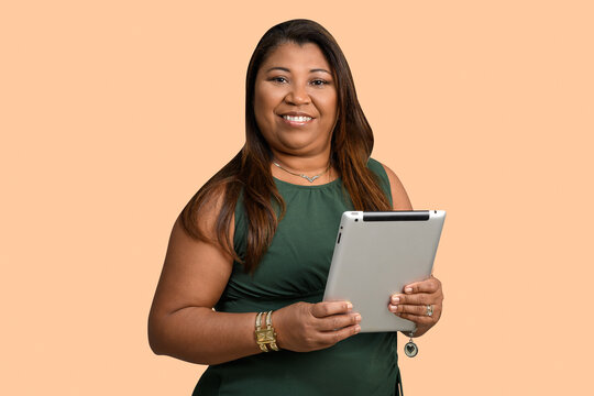 A smiling professional woman holds a tablet against a peach-colored background. - Powered by Adobe