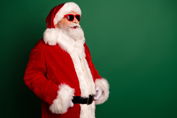 Santa Claus in red suit with white fur and hat wearing stylish shades against green background ready for Christmas shopping