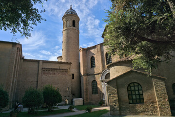 View of a cylindrical bell tower (Campanile) and basilica structure in Ravenna, framed by trees.