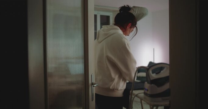 Woman folding freshly ironed clothes in softly lit room during evening, representing domestic care, focus, and calm routine in everyday home life - Powered by Adobe