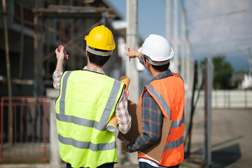 Two engineers wearing safety vests and helmets point toward the construction site for inspection.