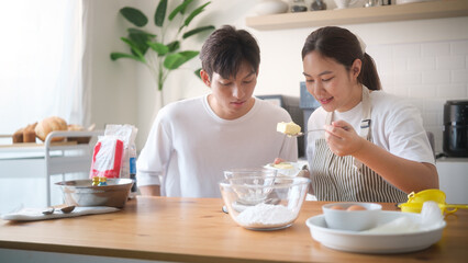 Couple preparing ingredients for baking in a cozy kitchen, woman measuring butter while man watches attentively. Concept of teamwork and home cooking.