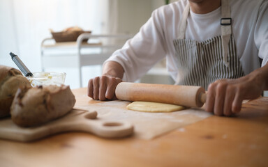 Close-up of man rolling dough on wooden table while baking at home. Concept of homemade cooking and artisan bread making.