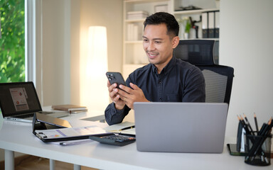 Professional man multitasking between laptop and smartphone in bright office.