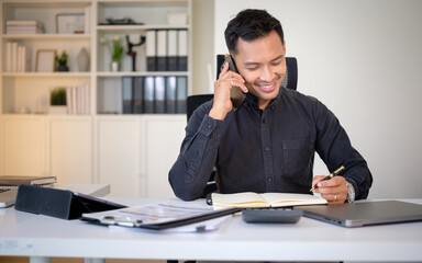 Professional man multitasking in office, making a phone call and writing in notebook.