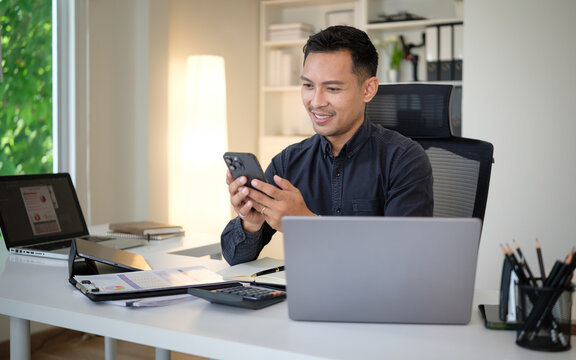 Professional man multitasking between laptop and smartphone in bright office. - Powered by Adobe