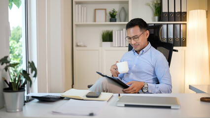 Smiling professional reads on a tablet during a coffee break in a tidy home office.