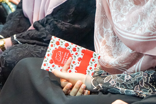 Johor, Malaysia, October 18, 2025: A person reads a bilingual religious booklet listing Islamic scholars, dressed in black attire, during a formal or spiritual gathering.