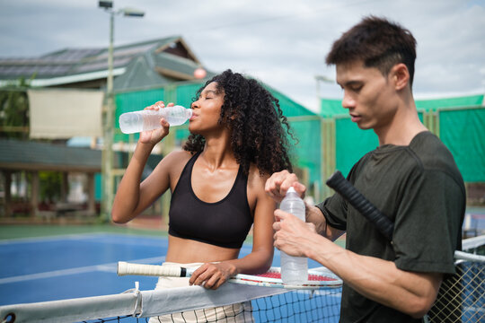 Two tennis players taking a water break after a match on an outdoor court. - Powered by Adobe