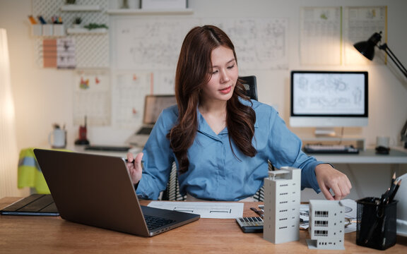 Female architect reviewing building models and blueprints at her modern workspace. - Powered by Adobe