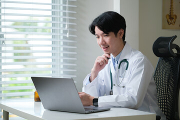 Male doctor in white coat consulting online through a laptop at his desk.