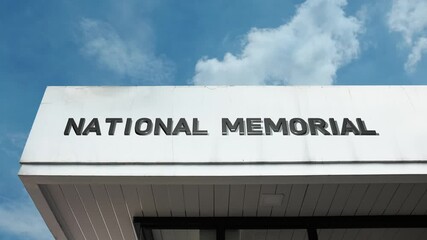 A National Memorial word sign displayed on a solemn, commemorative structure under a clear blue sky, symbolizing national remembrance, historical tribute, and respect