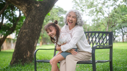 Fototapeta premium Elderly woman embraces young girl in a warm hug while laughing together in a park setting.