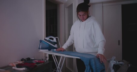 Woman ironing jeans in calm home environment, showing focus, domestic responsibility, and quiet perseverance in evening household routine