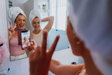 Two happy women taking selfie with under eye patches and towels on their heads