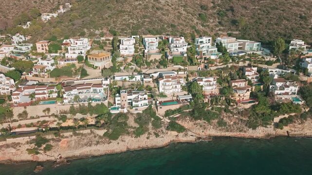 Drone footage of luxury cliffside villas with swimming pools in Moraira, Costa Blanca, Spain. Scenic Mediterranean coastline with elegant architecture and turquoise sea.