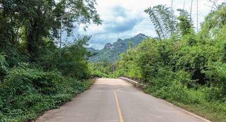 Quiet mountain road crossing a forest bridge under cloudy skies, surrounded by lush greenery and peaceful wilderness.