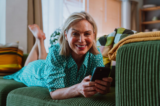 Smiling senior woman relaxing on sofa using smartphone at home