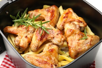 Grilled chicken wings with french fries and rosemary in air fryer basket on table, closeup
