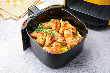 Grilled chicken wings with french fries and rosemary in air fryer basket on grey table, closeup